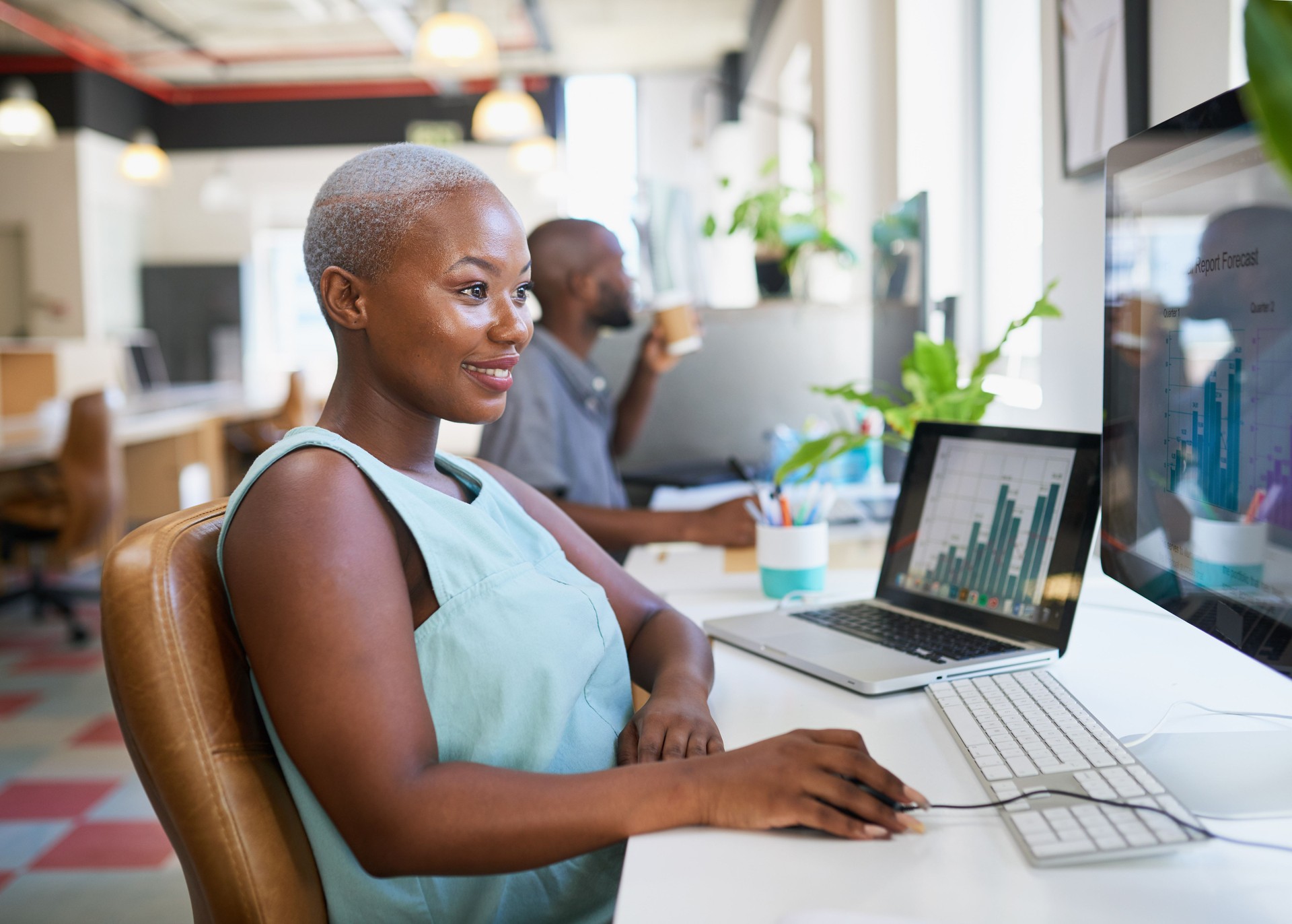 A young Black woman works on a financial forecast report in open plan office